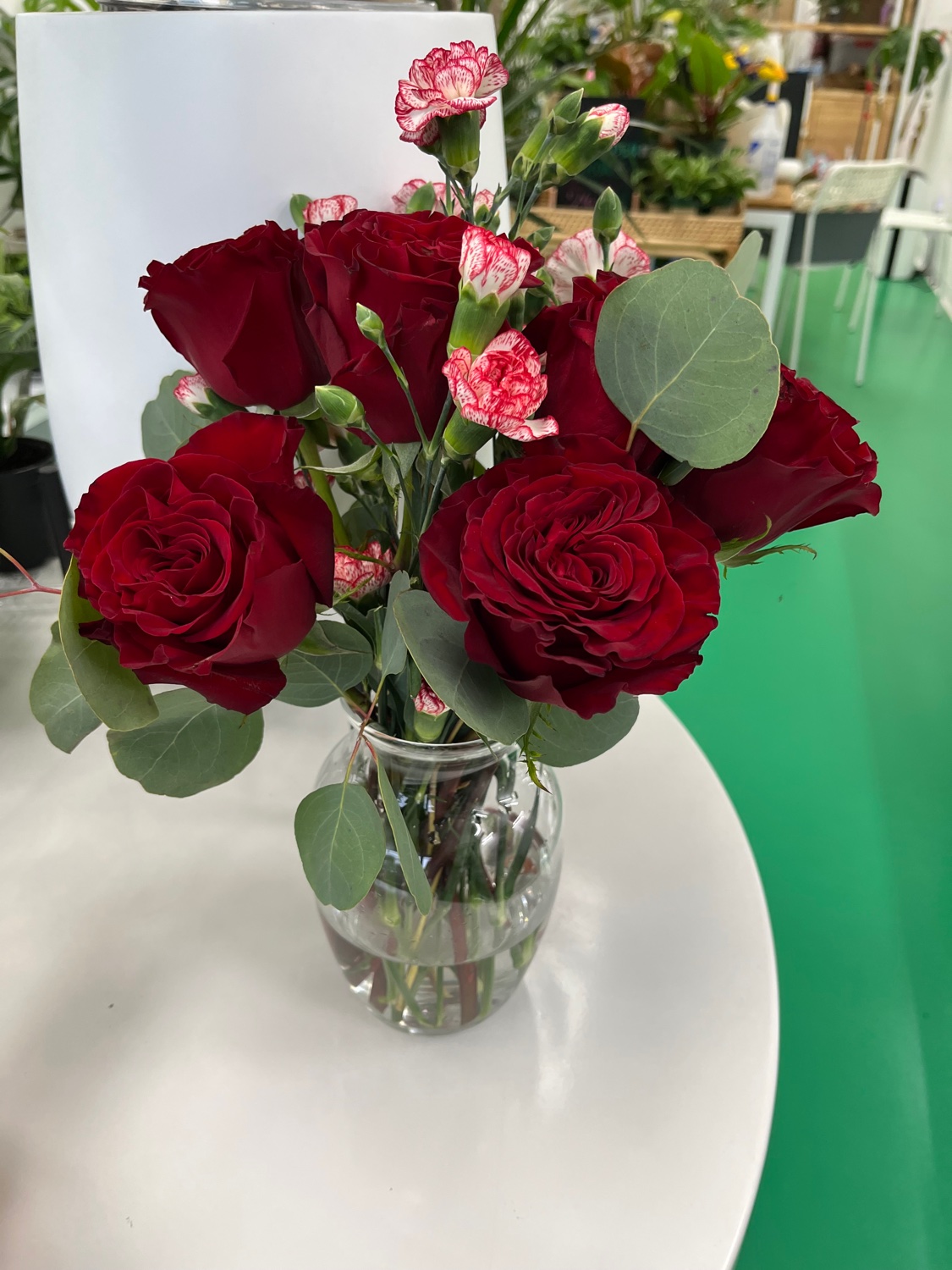 Rose bouquet in a clear glass vase with deep red roses, eucalyptus, and red-and-white mini carnations